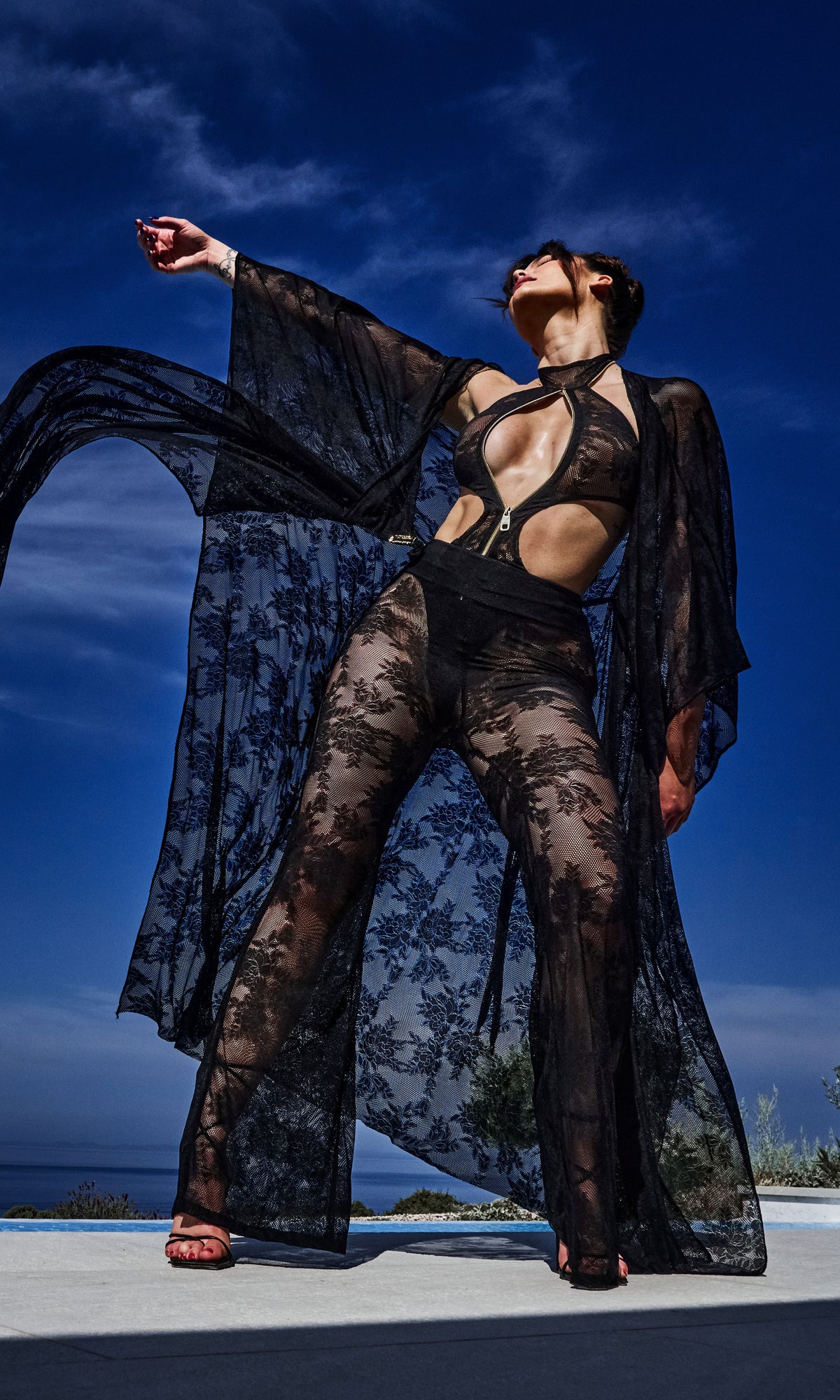 Model wearing Flora luxury sustainable sheer lace pants by Antoninias, designed with wide-leg silhouette and intricate floral detailing for premium resort wear and designer womenswear